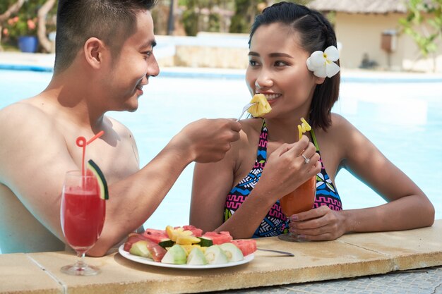 Asian man feeding girlfriend sliced fruit at tropical resort