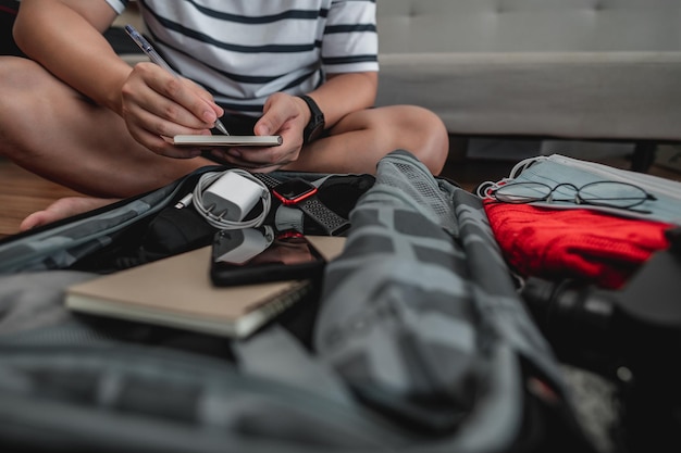 Asian man is preparing clothes in suitcases He's choosing clothes travel documents the itinerary for a solo trip and check the checklist Travel holiday and vacation concept