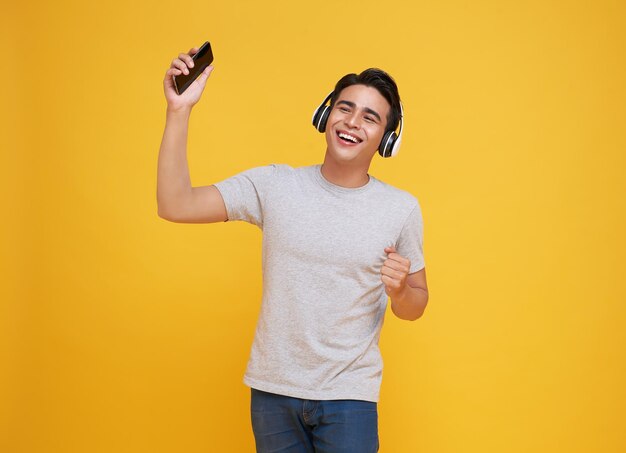 Asian man listening music playlist on moblie phone application with wireless headphones and dancing