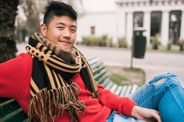 Free photo asian man sitting on a bench in park.