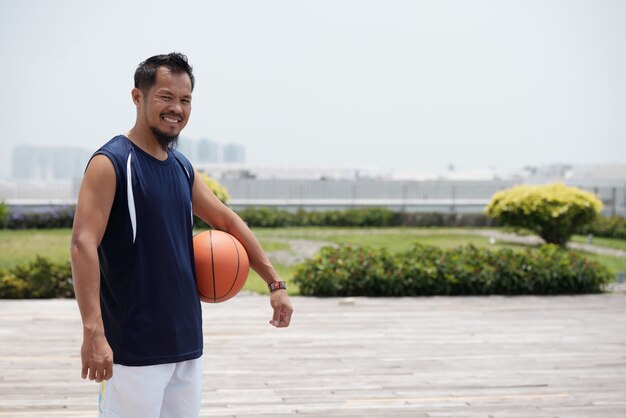 スタジアムで屋外に立って、バスケットボールを押しながら笑顔のアジア人