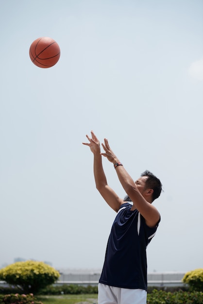 Asian man standing outdoors at stadium and throwing baseball up in air