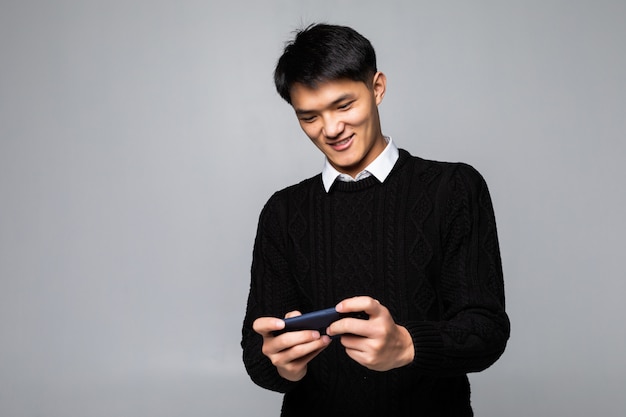 Asian man using the cellphone for playing game isolated on gray wall