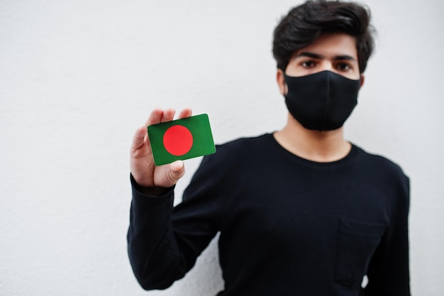 아시아 남성은 얼굴 마스크를 쓴 검은색 옷을 입고 코로나바이러스 국가 개념에 격리된 손에 방글라데시 국기를 들고 있다