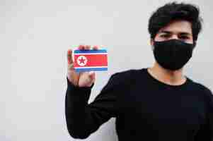 Free photo asian man wear all black with face mask hold north korea flag in hand isolated on white background coronavirus country concept