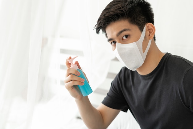 Asian man wearing Face Mask holding Alcohol for washing hands to protect Coronavirus covid-19 in quarantine room 