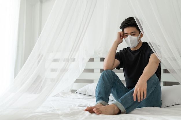 Азиатский мужчина носит маску для лица для защиты от головной боли и кашля из-за коронавируса covid-19 в карантинной комнате
