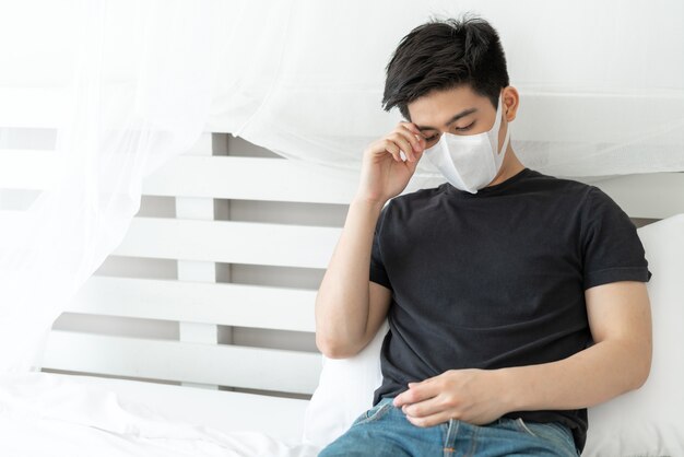 Asian man wearing Face Mask to protect  feeling sick headache and cough because of Coronavirus covid-19 in quarantine room 