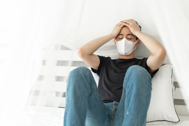 격리실에서 코로나 바이러스 COVID-19로 인해 아픈 두통과 기침을 보호하기 위해 얼굴 마스크를 착용 한 아시아 남자