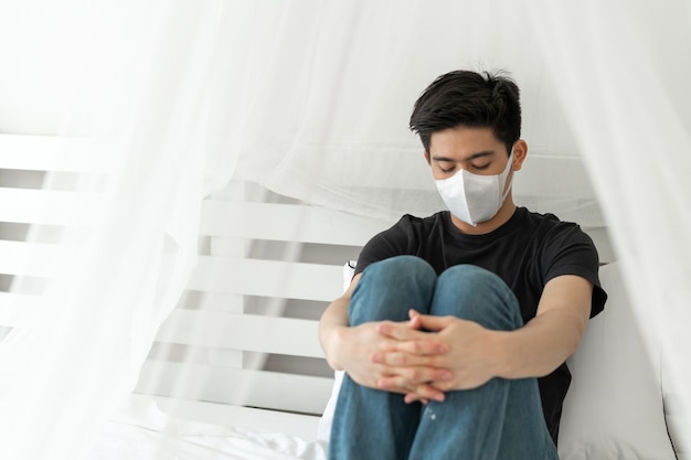격리실에서 코로나 바이러스 COVID-19로 인해 아픈 두통과 기침을 보호하기 위해 얼굴 마스크를 착용 한 아시아 남자