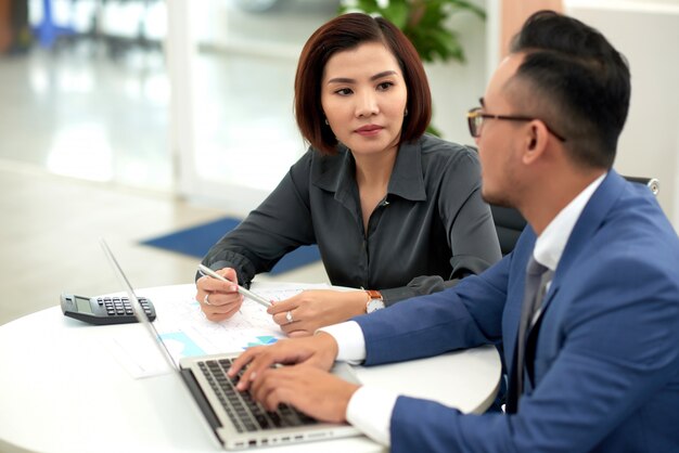 asian man and woman in business attire sitting at table indoors and talking