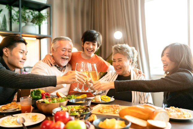 Азиатские дедушки и бабушки из нескольких поколений, внуки, счастье, радостный ужин вместе на праздновании домашних праздников и концепция людей, счастливые друзья с бенгальскими огнями, ужинающие в честь Рождества