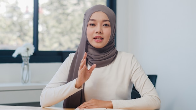 カメラを見ているアジアのイスラム教徒の女性は、新しい通常のオフィスでのビデオ通話の計画について同僚に話します。