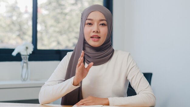 Asian muslim lady looking at camera talk to colleagues about plan in video call in new normal office.