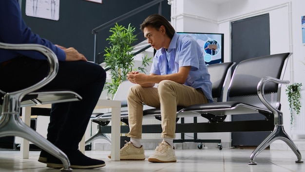 Free photo asian patient being stressed and tired during checkup visit appointment while waiting for specialist to discuss health care treatment. young adult sitting on chair in hospital waiting room.