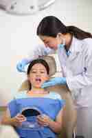 Free photo asian patient sitting with open mouth and holding mirror, and dentist checking her teeth