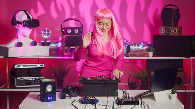 Free photo asian performer dancing and interacting with fans in club at nightime, playing electronic remix at professional mixer console. artist with pink hair mixing sounds using audio equipment
