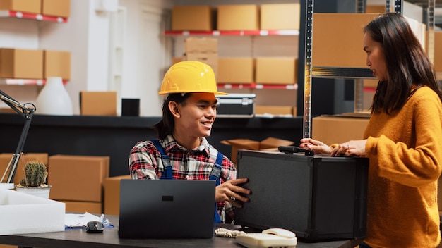 Asian person checking warehouse supplies from shelves, using supply chain production to work on inventory on laptop. Young man planning shipment for startup business development.