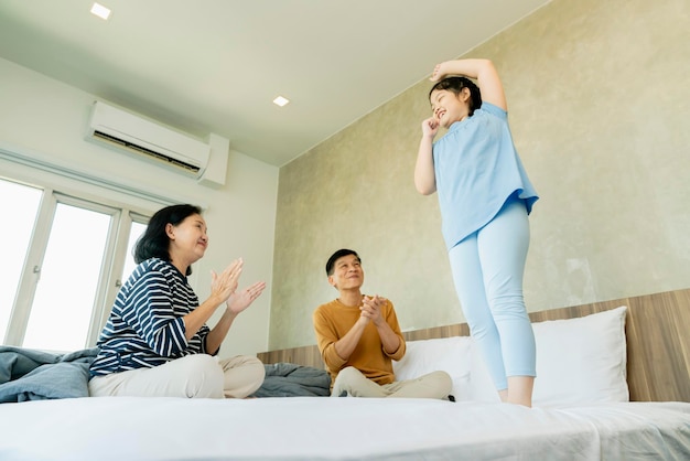 Asian Senior grandparents couple laying with grandchildren preety female child on bed in bedroomhappy family play together in the bed