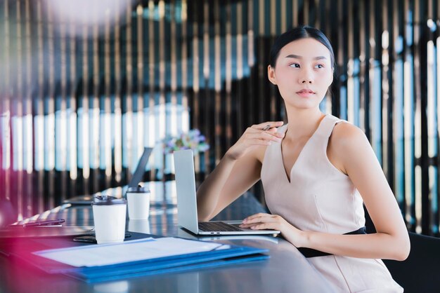 アジアのスマートbusineswomanは仕事をし、幸福と新鮮さのオフィスの背景を持つスマートフォンやラップトップと通信します