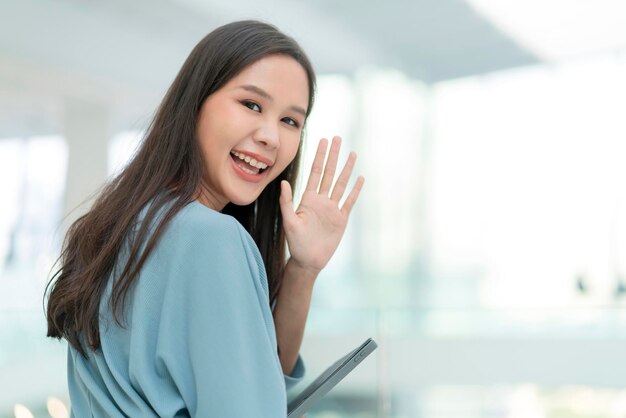 Asian smiling cheerful female digital nomad hand hold tablet device look at camera portrait shothappiness smiling asia woman standing in office college corridor with positive smiling attitude