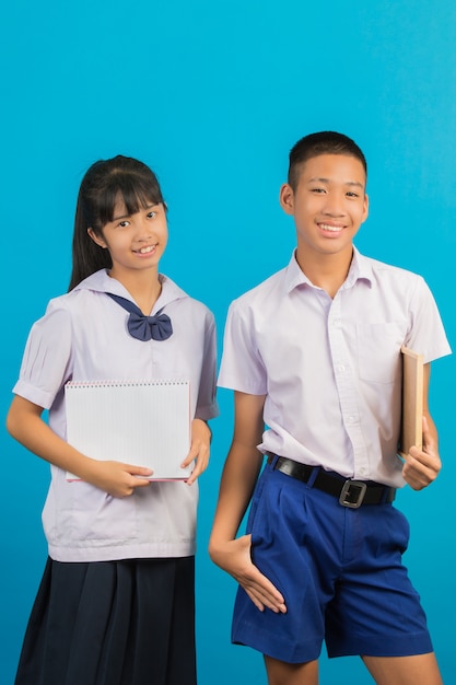 An Asian student holding a notebook andAsian male student holding a green board on a blue .