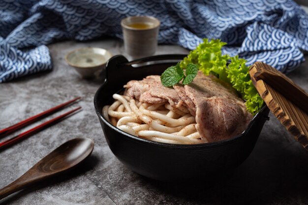 Asian style soup with noodles, pork and green onions closely in a bowl on the table.