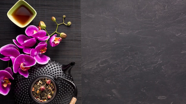 Asian tea set with orchid flower and dried tea ingredient on black place mat