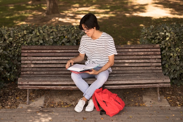 Asian teen man with textbook on bench