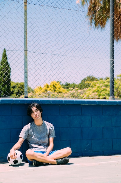 Азиатский подросток студент сидит возле забора спортплощадки
