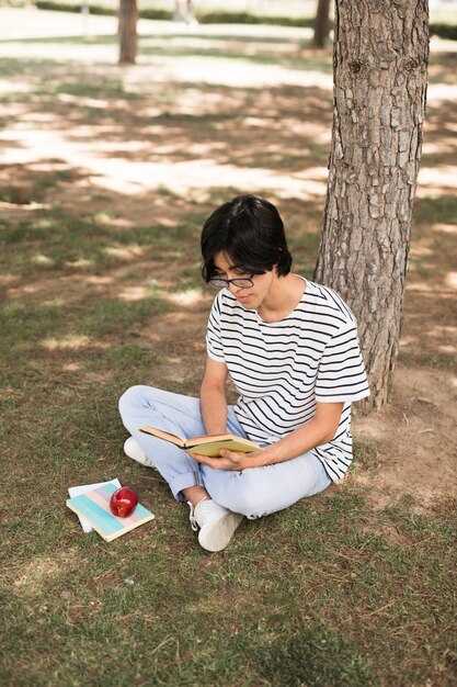Asian teenage student reading book under tree