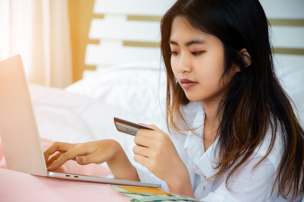 Asian teenage woman use laptop and credit-card on bed