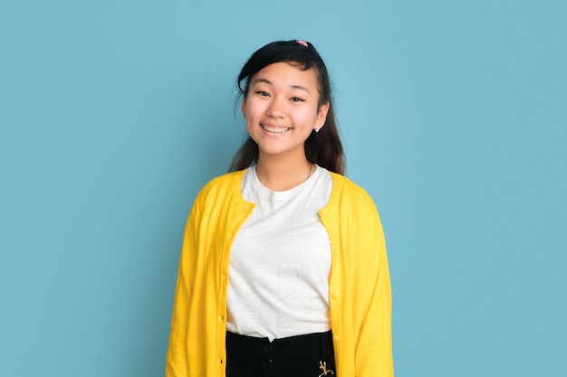 Asian teenager's portrait isolated on blue studio background. Beautiful female brunette model with long hair in casual style. Concept of human emotions, facial expression, sales, ad. Smiling cute.