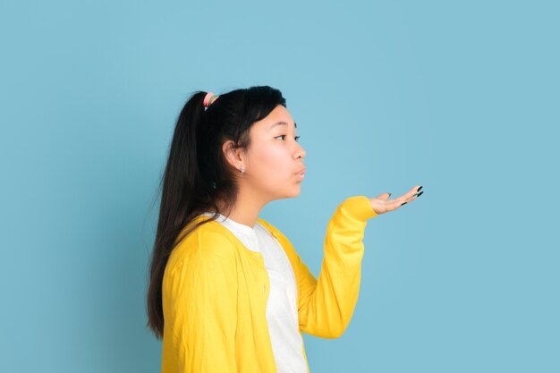 Asian teenager's portrait isolated on blue studio background. Beautiful female brunette model with long hair. Concept of human emotions, facial expression, sales, ad. Sending kisses, looks cute.