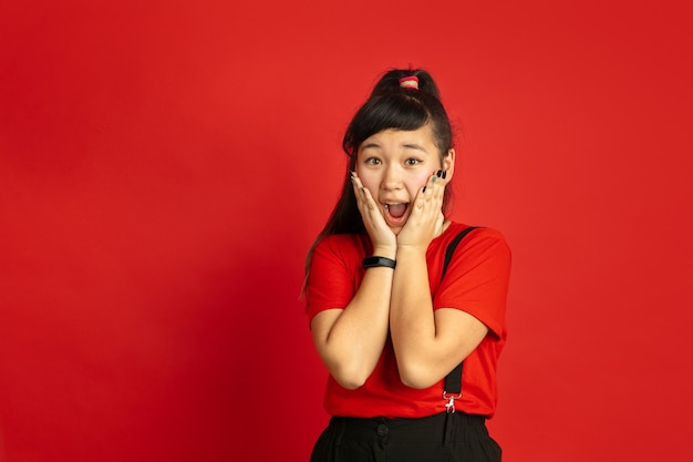 Foto gratuita ritratto di adolescente asiatico isolato su sfondo rosso studio. bello modello femminile del brunette con i capelli lunghi in casuale. concetto di emozioni umane, espressione facciale, vendite, annuncio. stupito, scioccato.