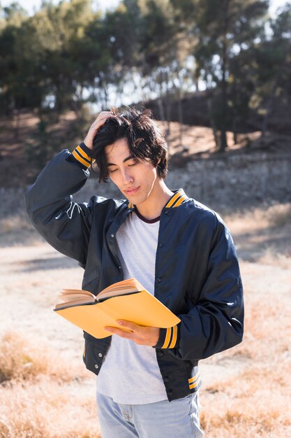 Asian teenager scratching head and reading book in park