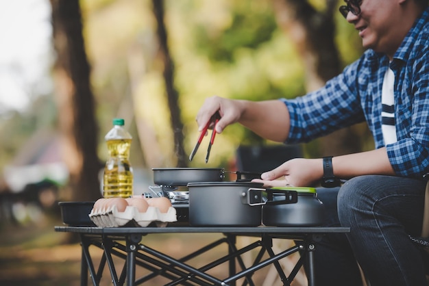 Occhiali da uomo viaggiatore asiatico che friggono un gustoso uovo fritto in una padella calda al campeggio cucina all'aperto concetto di stile di vita in campeggio in viaggio