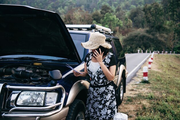 Asian woman calling repairman or insurance staff to fix a car engine problem on a local road 