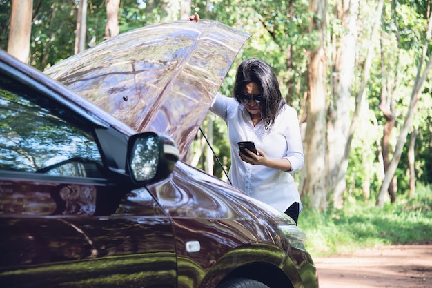 Asian woman calling repairman or insurance staff to fix a car engine problem on a local road 