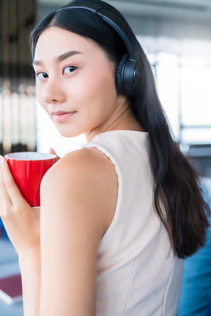 Азиатская женщина в повседневной рабочей одежде делает перерыв с кофе и журналом на диване на домашнем фоне гостиной