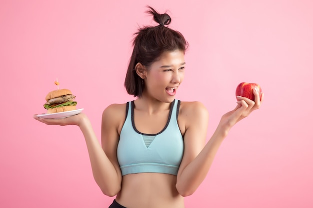 Азиатская женщина, выбирая между гамбургером и красное яблоко на розовом