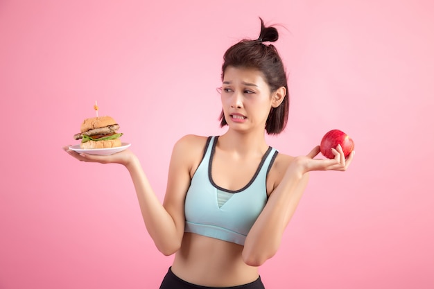 asian woman choosing between hamburger and red apple on pink