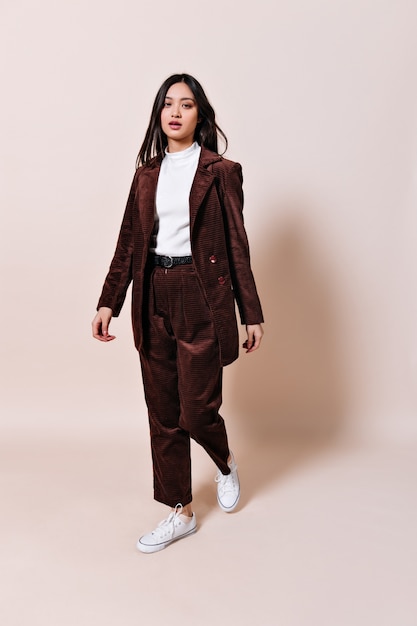 Asian woman in corduroy suit looks into front on beige wall