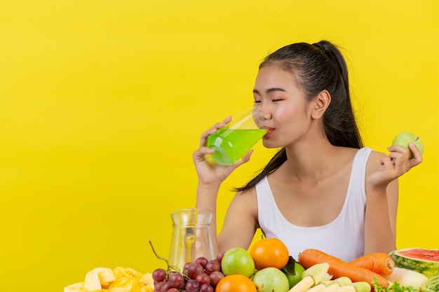 Donna asiatica che beve il succo di mela e sul tavolo ci sono molti frutti.