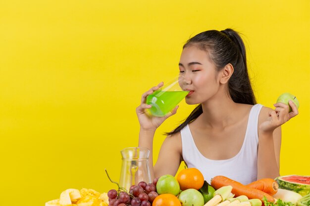 アジアの女性はリンゴジュースを飲むし、テーブルの上には多くの果物があります。