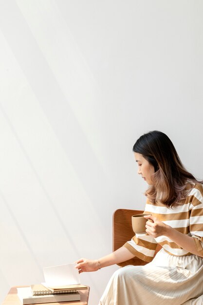 Free Photo asian woman drinking coffee while reading a book at home