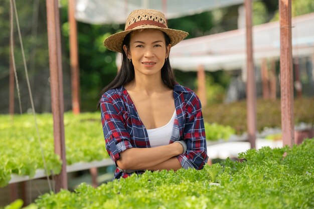 幸せそうに野菜の水耕栽培で働くアジアの女性農家。グリーンハウス農場で、グリーンサラダ野菜の品質を笑顔でチェックする女性農家のポートレート。