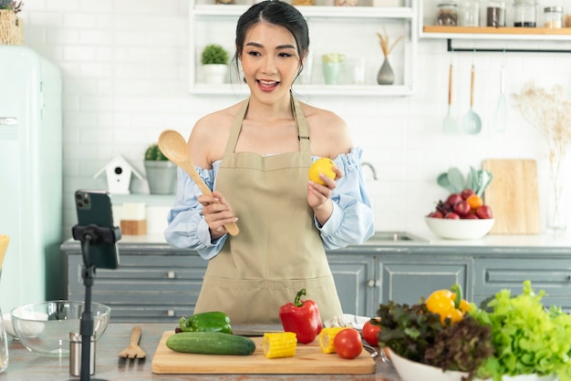 Asian woman food blogger cooking salad in front of smartphone camera while recording vlog video