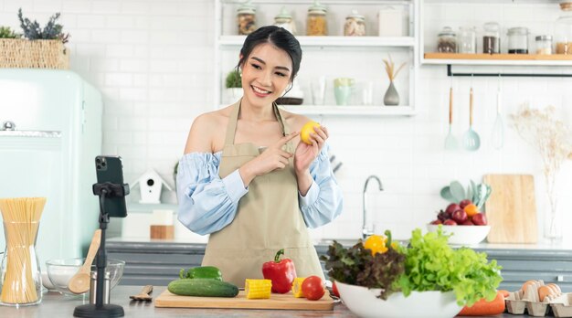 Asian woman food blogger cooking salad in front of smartphone camera while recording vlog