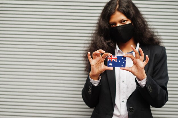 Asian woman at formal wear and black protect face mask hold Australia flag at hand against gray background Coronavirus at country concept